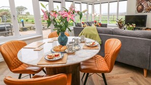A modern living room with a dining area, large windows, and a view of the outdoors. - Meadowside (Penzance)