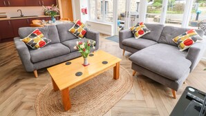 A modern living room with two grey sofas, a wooden coffee table, and a vase of flowers. - Meadowside (Penzance)