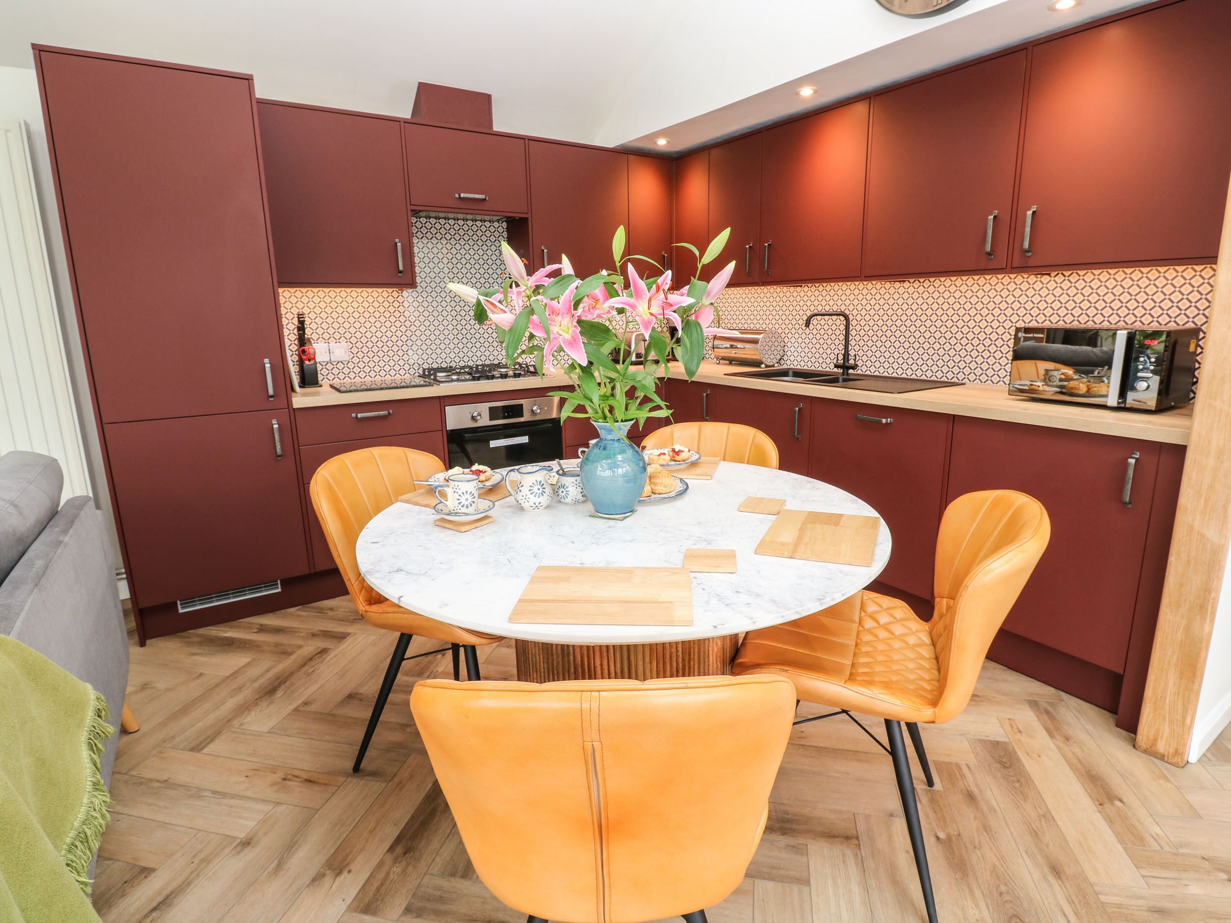 A compact kitchen with modern appliances, a dining table with chairs, and a vase with flowers.