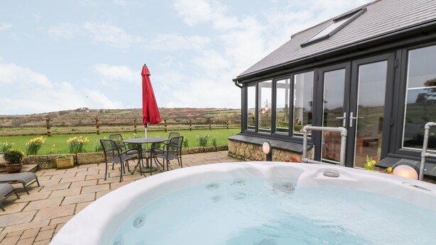 A hot tub with a view of a green field and a red umbrella. - Meadowside (Penzance)