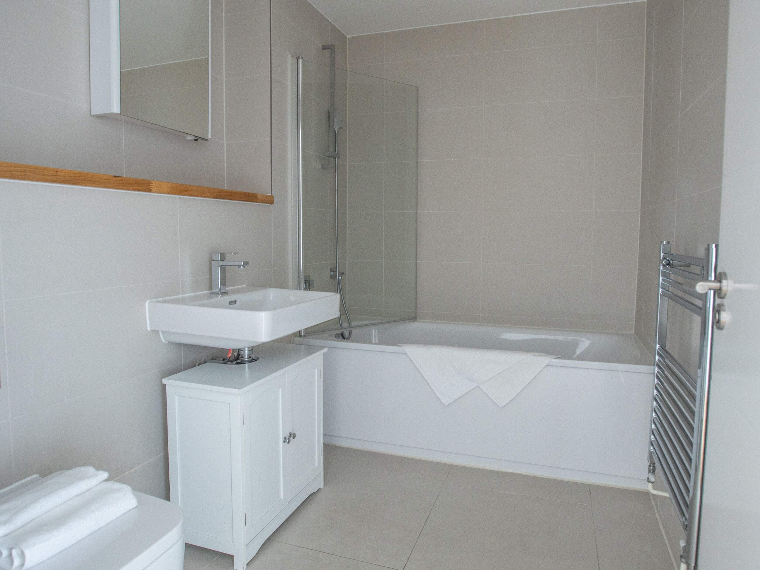 Un baño moderno con un lavamanos blanco, una cabina de ducha de vidrio y una bañera blanca.