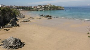 Una playa con afloramientos rocosos y una vista distante de un pueblo con edificios en una colina.