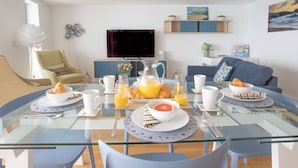 Un moderno salón con una mesa de vidrio dispuesta para el desayuno, una televisión y un sofá.