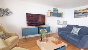 Una sala de estar moderna con un sofá, una mesa de centro con un juego de ajedrez, un televisor y una cocina al fondo.