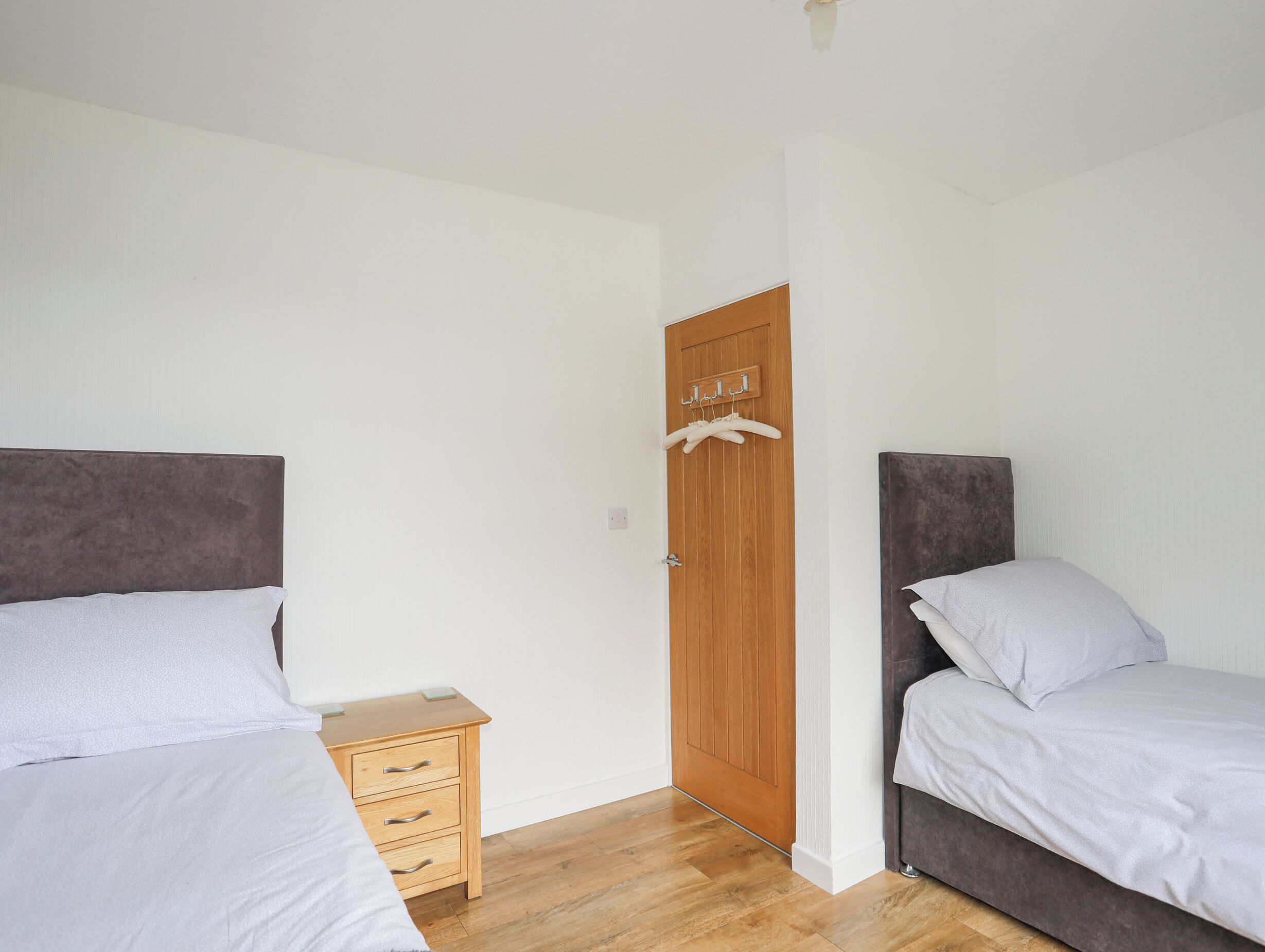 Een slaapkamer met twee bedden, een houten deur en een klein nachtkastje.