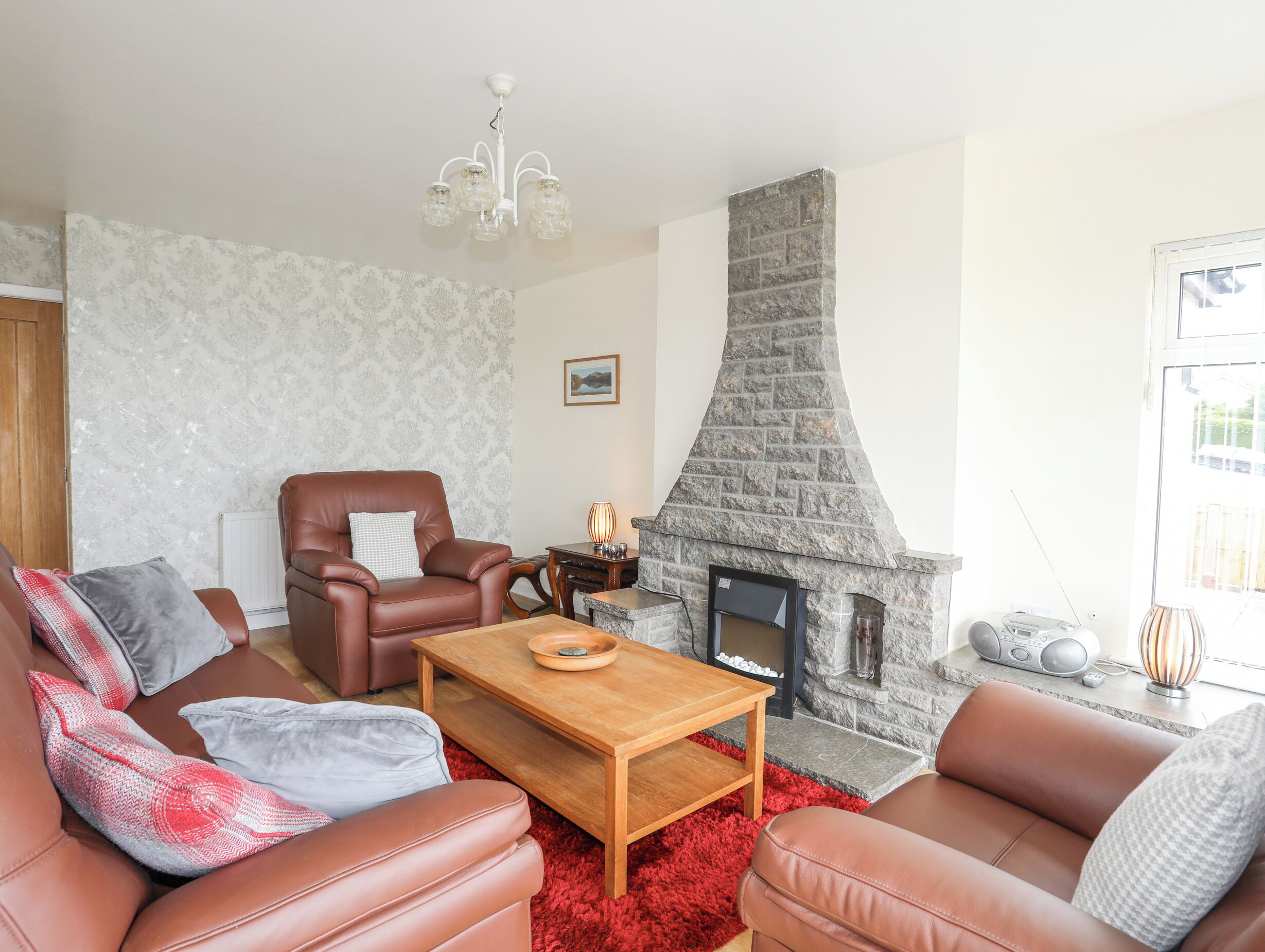 A living room with leather sofas, a wooden coffee table, a stone fireplace, and a chandelier.
