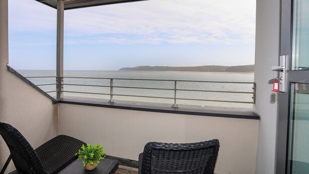 Ein Balkon mit Blick auf das Meer, ein Topfpflanze und zwei Korbstühle.
