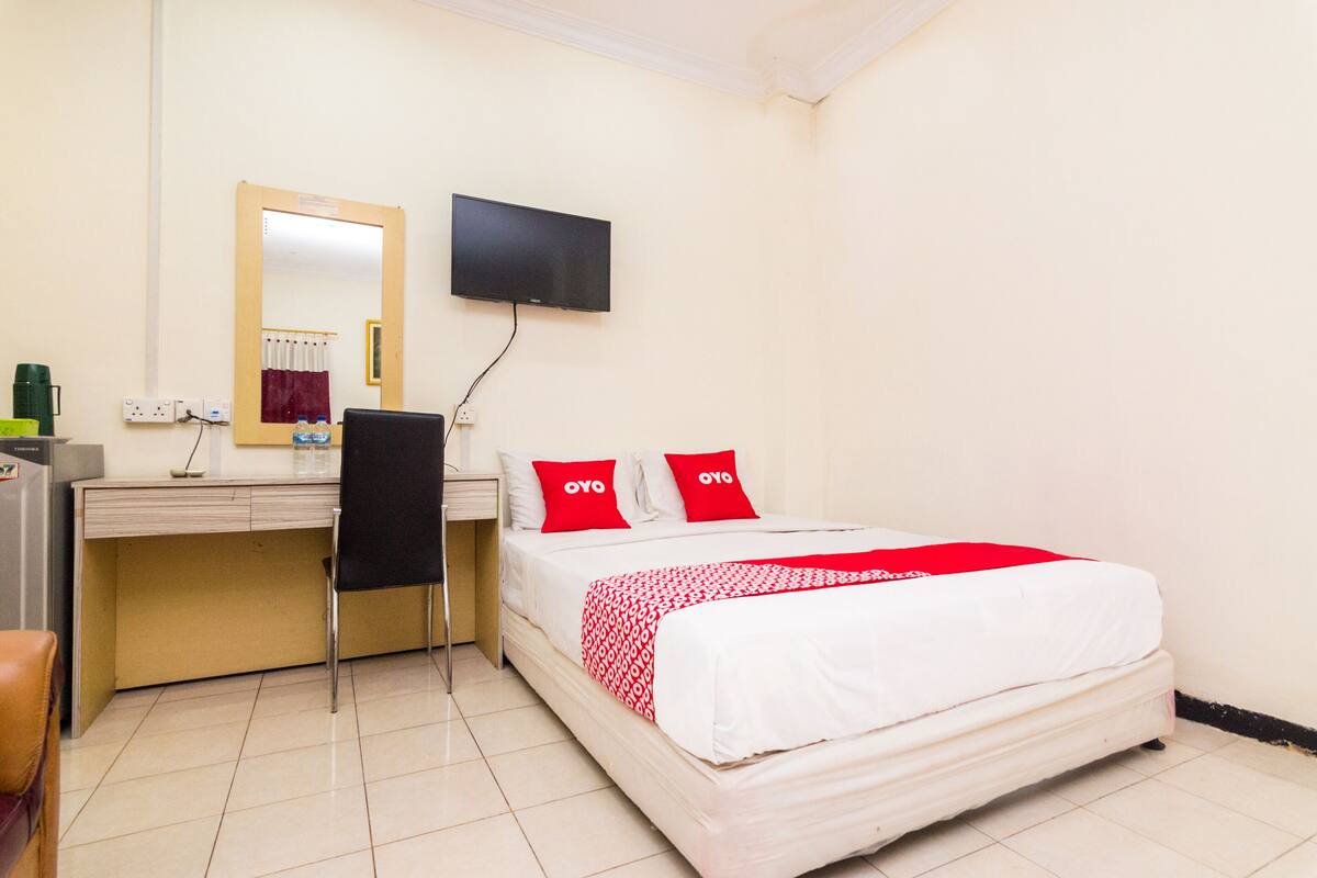 Une chambre d’hôtel avec un lit, un bureau, une chaise, une télévision et un miroir.