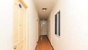 A narrow hallway with a wooden floor, beige walls, and a door with a blue sign. - OYO 2097 Hotel Laksana Inn (Batam)