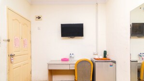 A small room with a wooden door, a desk with a chair, a television mounted on the wall, and a refrigerator. - OYO 2097 Hotel Laksana Inn (Batam)
