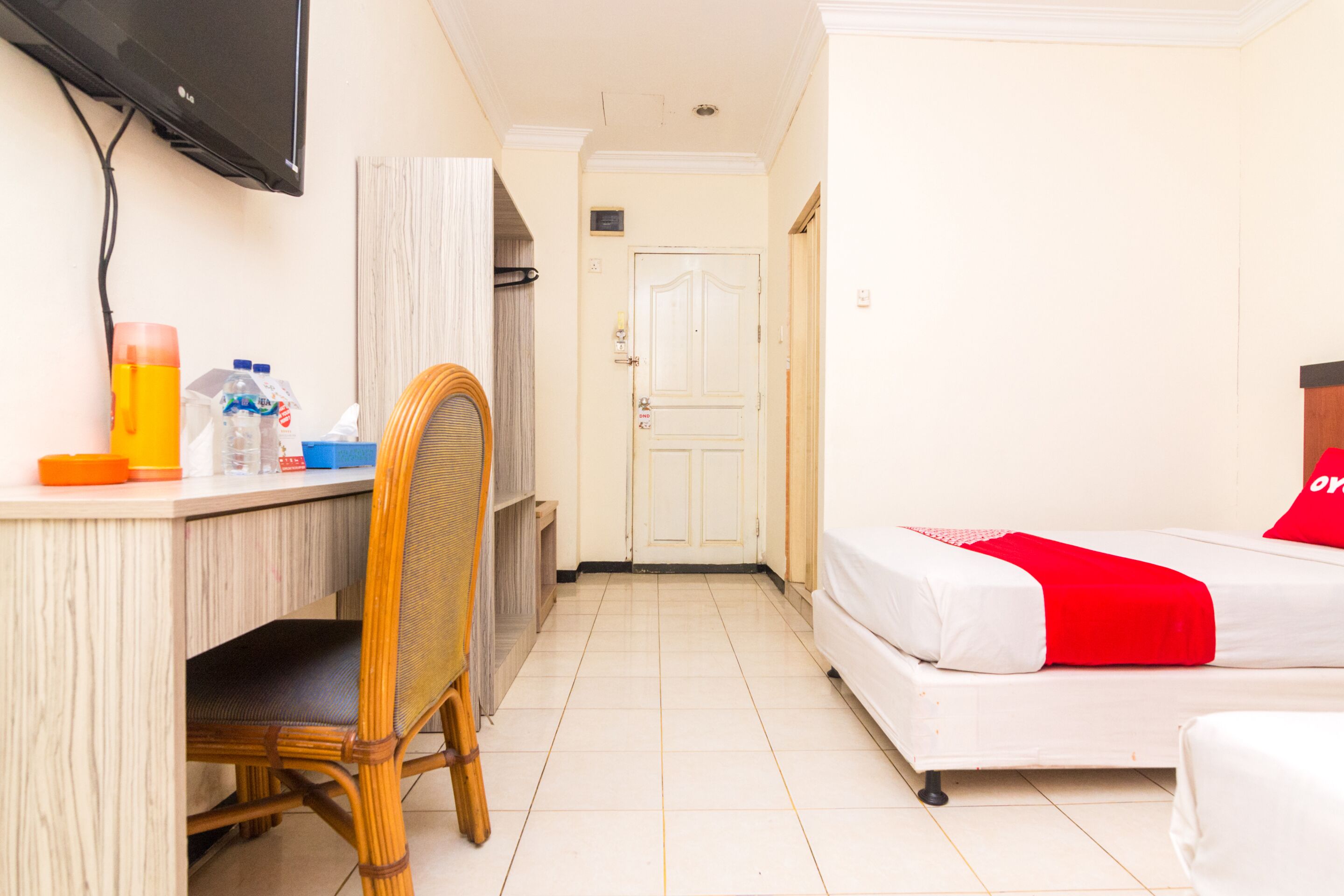 A hotel room with a bed, a desk, a chair, and a television mounted on the wall.