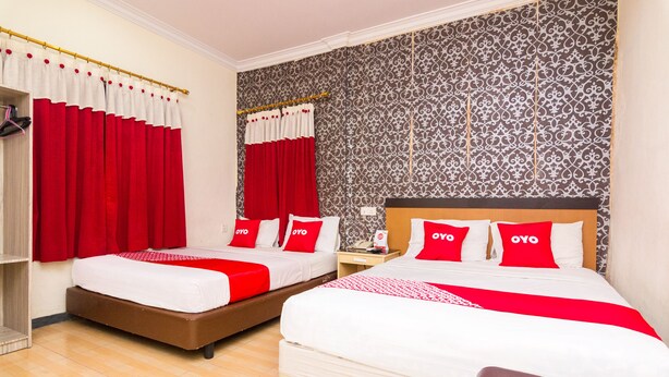 A hotel room with two beds, red and white bedding, a patterned wallpaper, and a wooden floor. - OYO 2097 Hotel Laksana Inn (Batam)