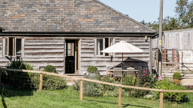 A rustic wooden building with a sloped roof, a wooden door, and a small patio area with a table and an umbrella.