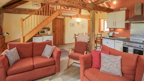 A rustic interior with wooden beams, a kitchen, and a dining area with red sofas and patterned cushions.