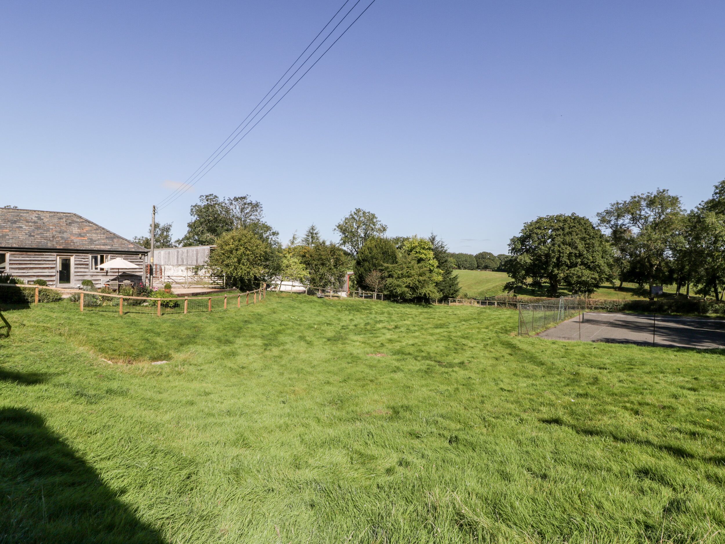 A grassy field with a wooden fence, a building with a sloped roof, and trees in the background.