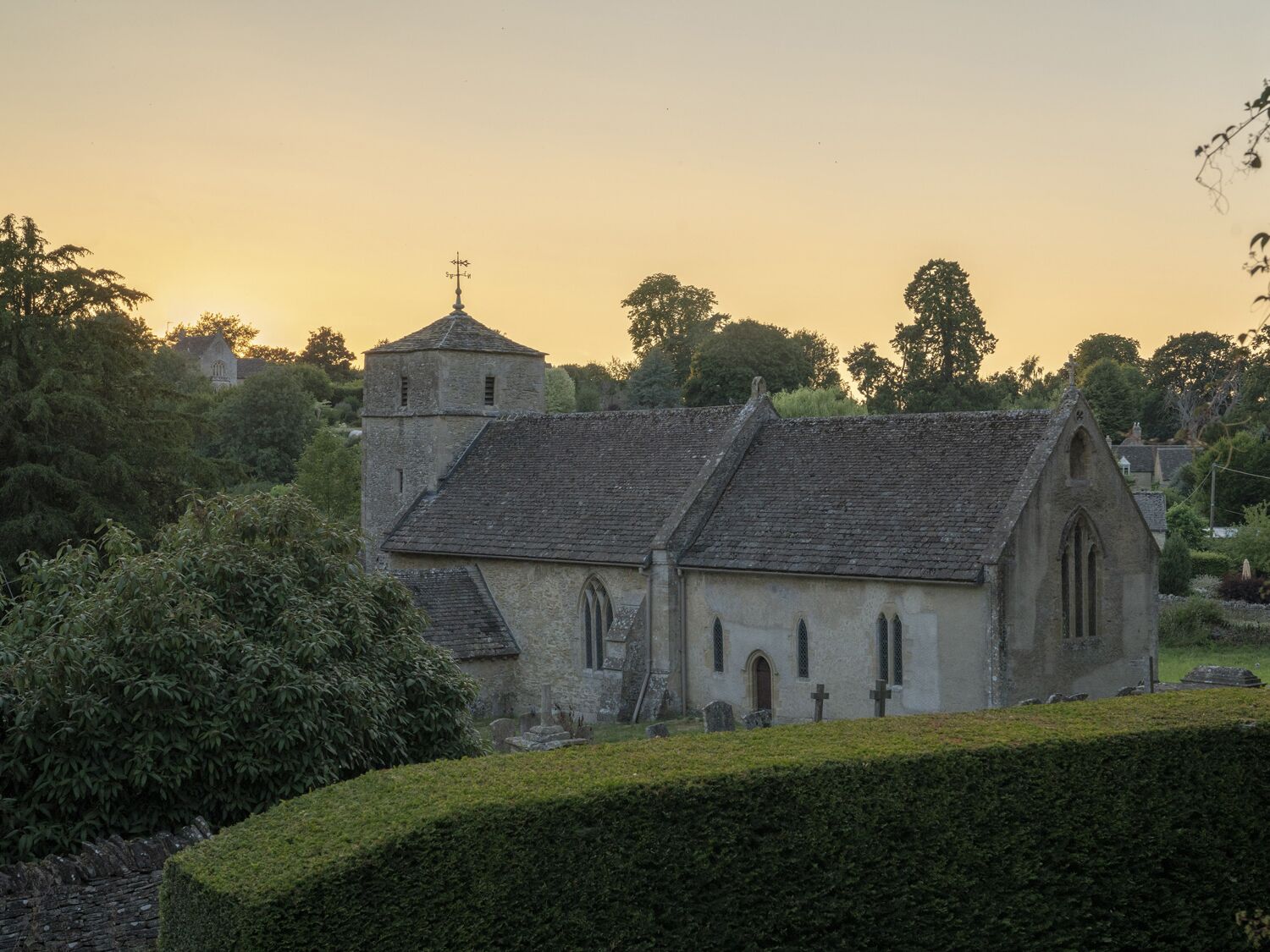 A church with a tower and a bell, surrounded by greenery and trees.