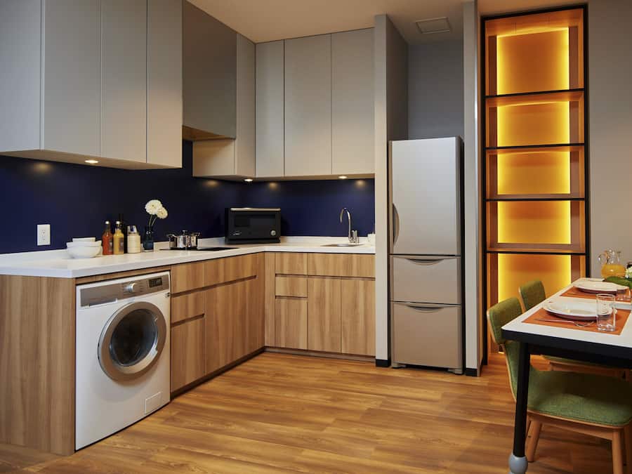 Eine moderne Küche mit Holzausstattung, einer eingebauten Waschmaschine, einem Kühlschrank und einem Essbereich mit Tisch und Stühlen.