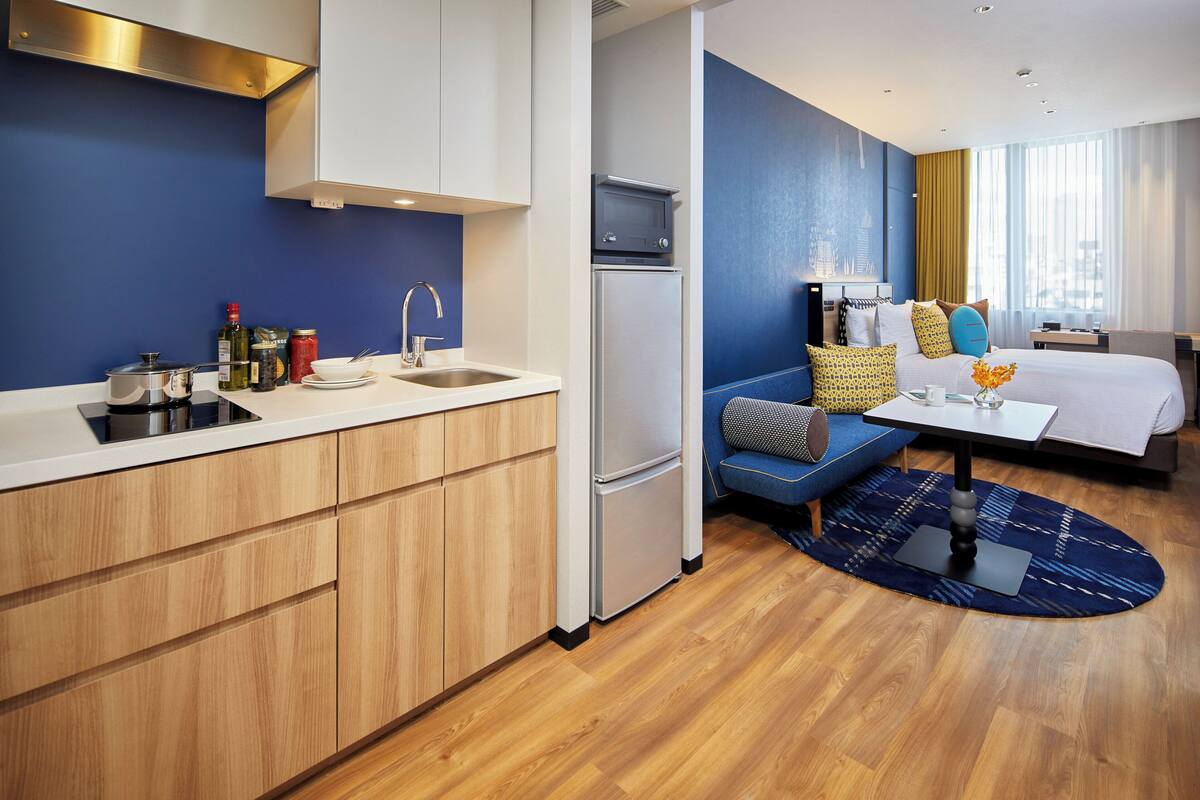 A modern hotel room with a kitchen area, a sofa bed, and a dining table.
