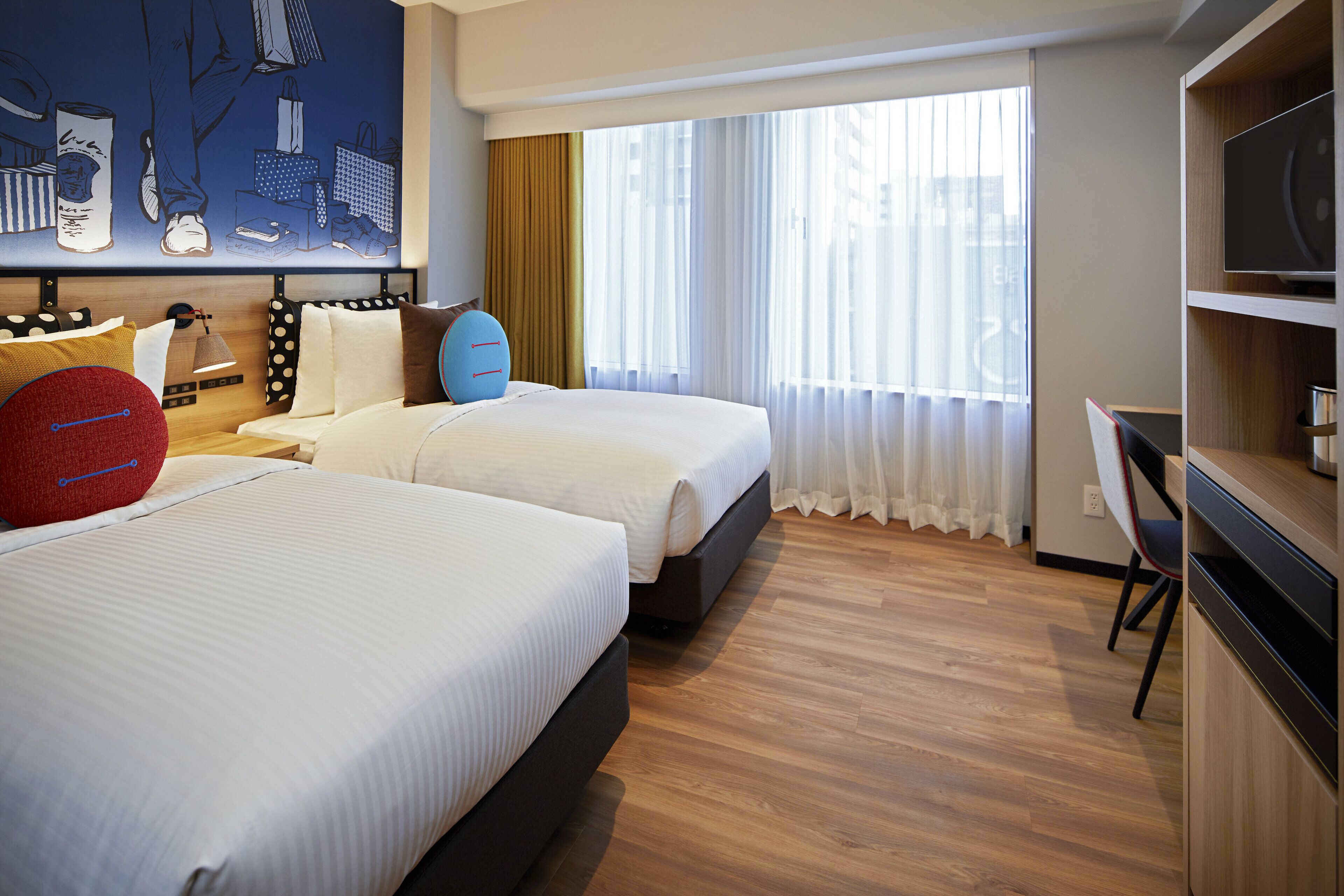 A hotel room with two beds, a TV, a desk, and a large window with curtains.