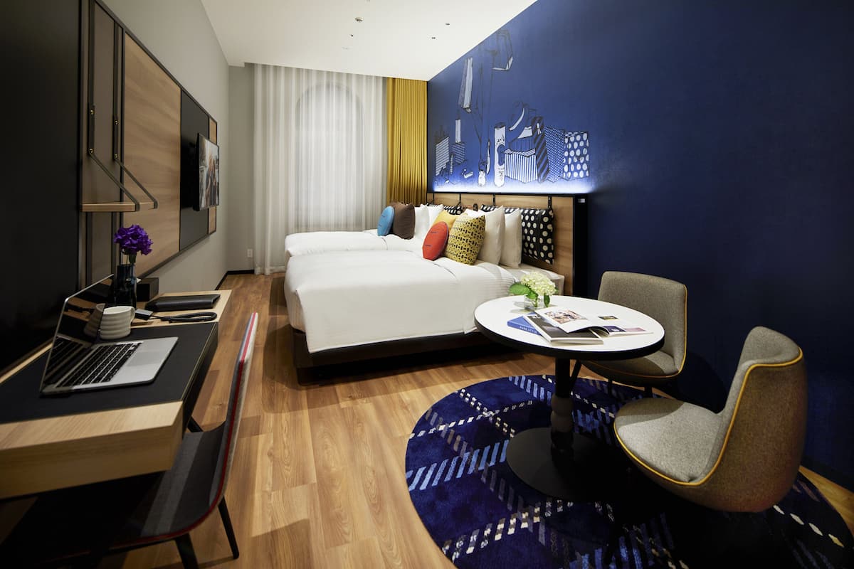 A modern hotel room with a bed, desk, laptop, chair, and a round table.