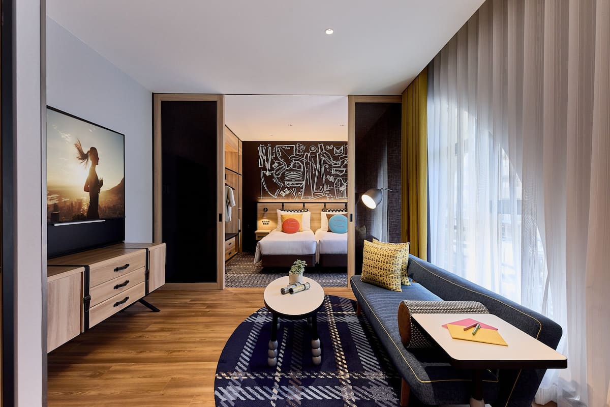 A modern hotel room with a large bed, a sofa, a desk, and a TV.