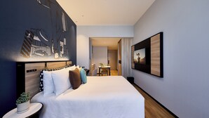 Una habitación de hotel moderna con una cama grande, un escritorio pequeño, una planta en maceta y un mural en la pared.