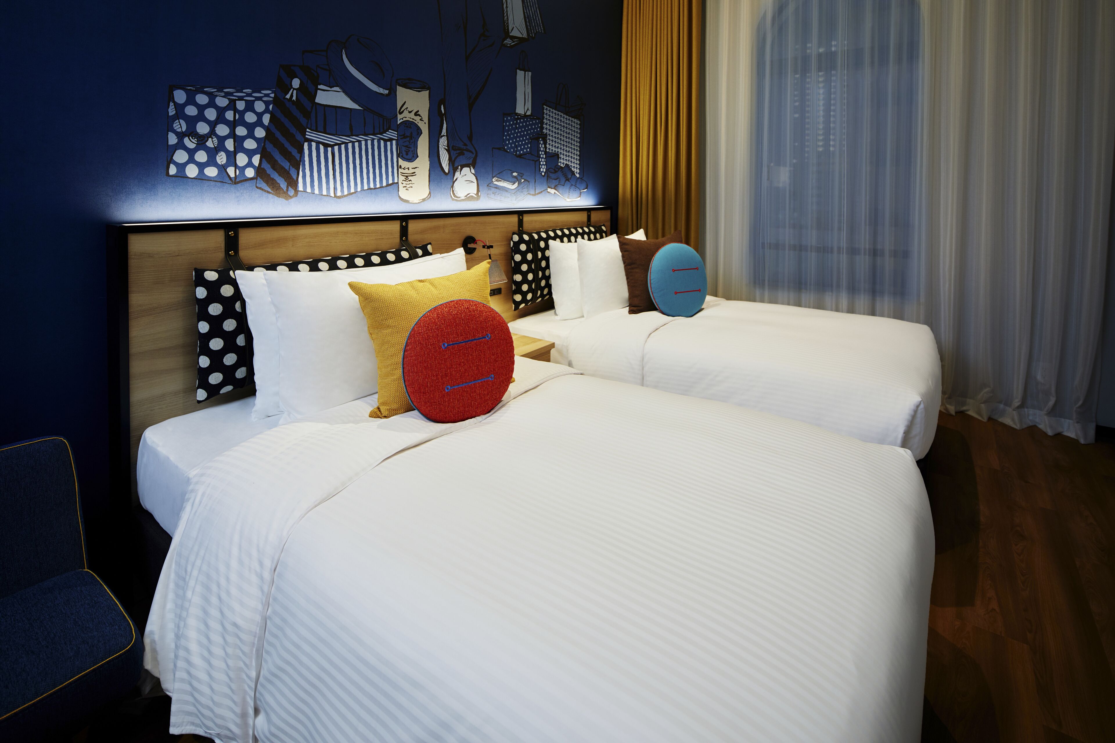 Una habitación de hotel con dos camas, un cabecero de madera y una obra de arte con un motivo urbano en la pared.