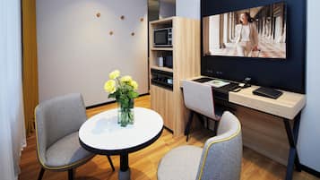 Una habitación de hotel moderna con una mesa redonda, dos sillas, un televisor y un armario de madera con estantes.