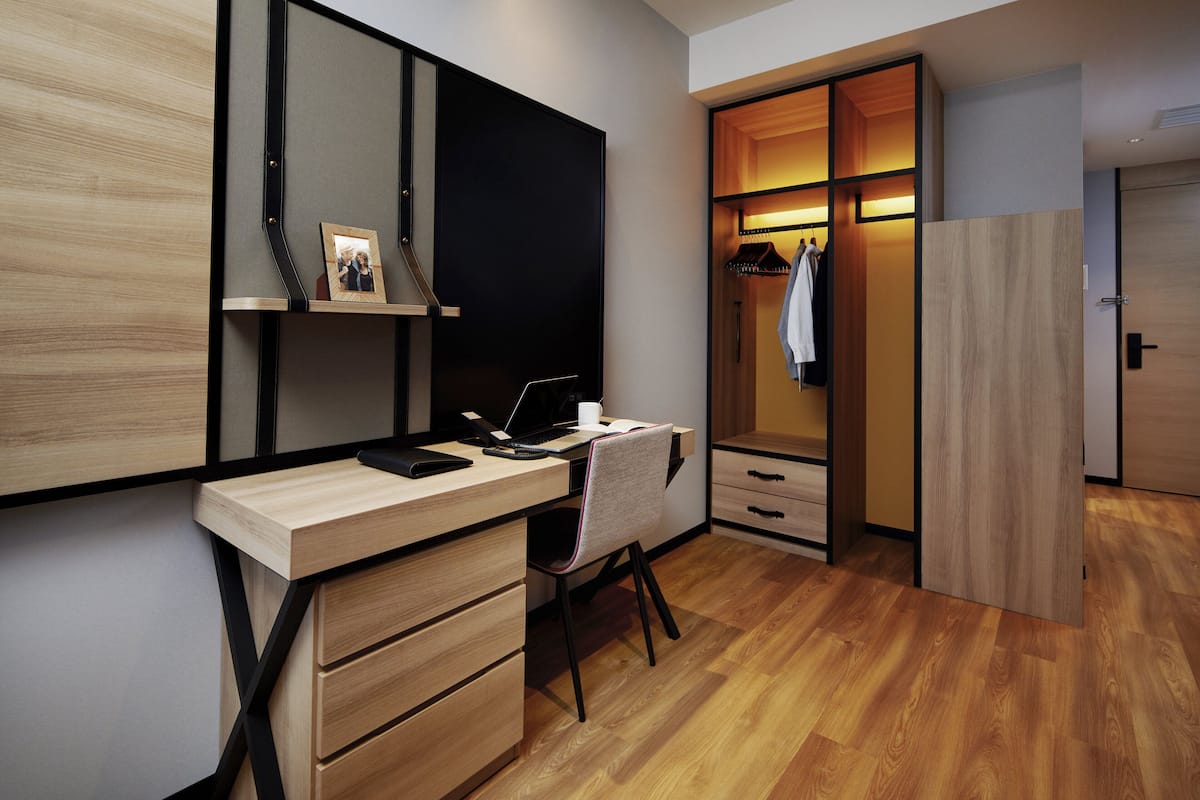 A modern bedroom with a wooden desk, a chair, a wardrobe, and a mirror.