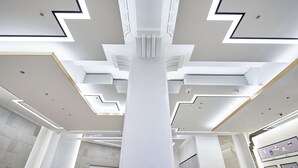 Un interior moderno con una columna central, iluminación empotrada y patrones geométricos en el techo.