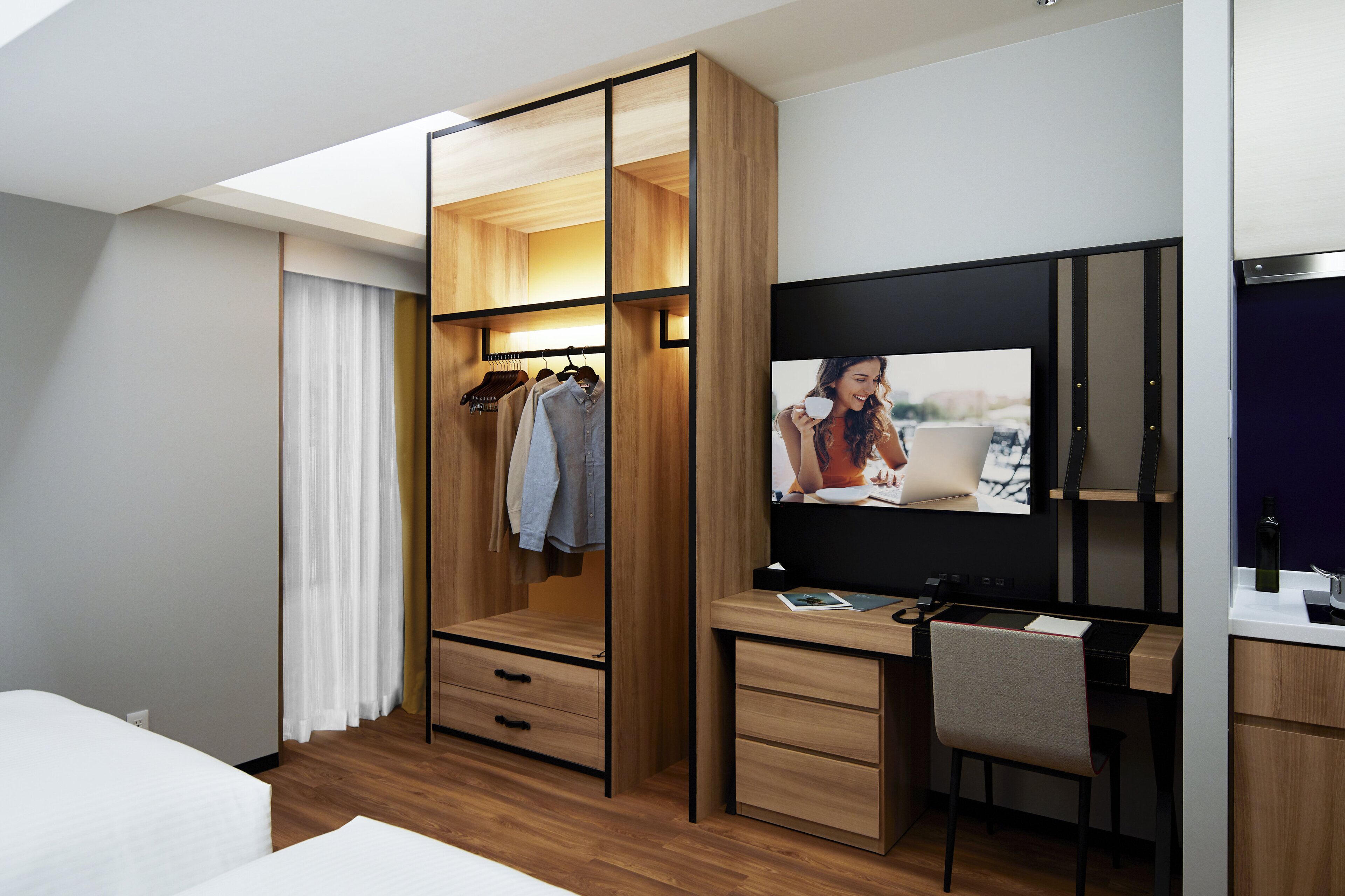 Une chambre d’hôtel moderne équipée d’une armoire en bois, d’un bureau avec une chaise, d’une télévision et d’un lit.