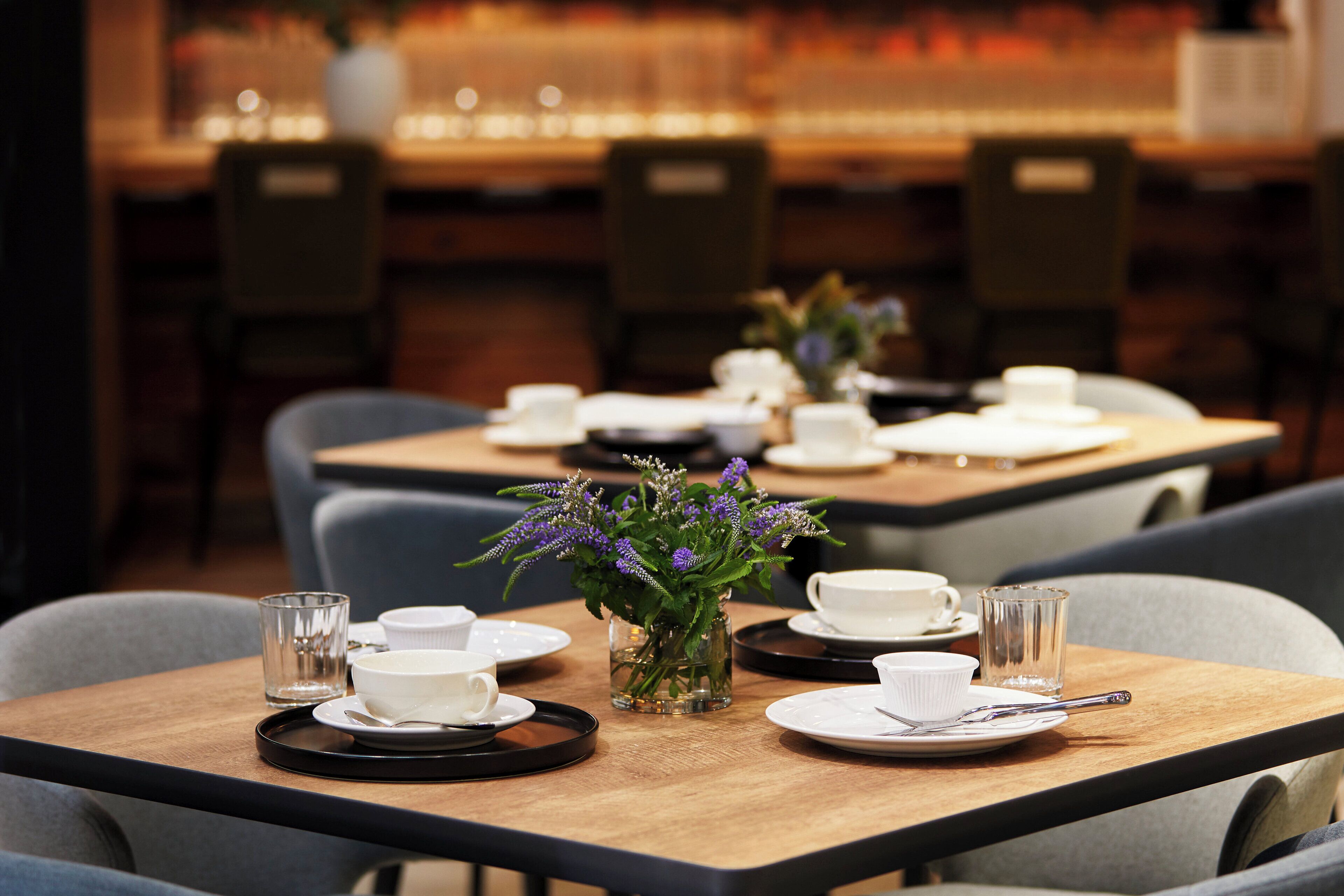 A dining area with tables set for tea service, featuring clear glassware and a vase with flowers.