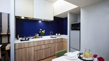A modern kitchen with wooden cabinets, a white countertop, and a sink. There is a dining table with a green chair and a tray with a pitcher of juice and a vase with flowers.