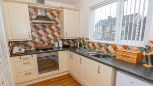 Een keuken met witte kastjes, een betegelde spatwand, een raam met zonwering en een houten broodkist.