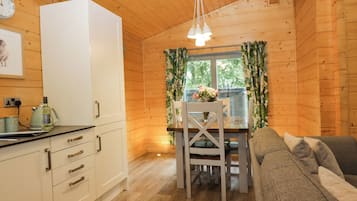 A cozy cabin interior with a dining table, chairs, a sofa, a white refrigerator, and a clock on the wall.