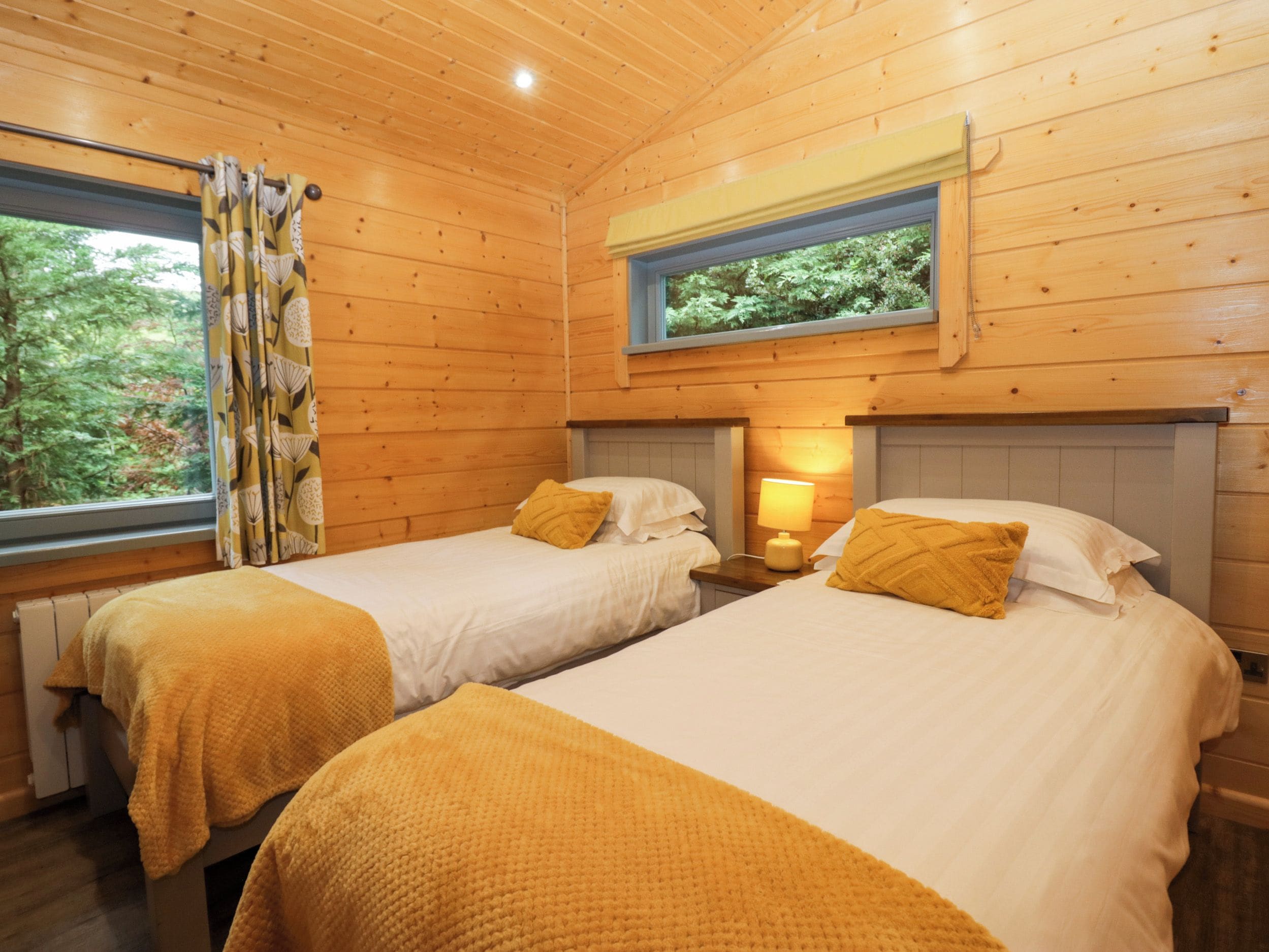 A cabin with two beds, each with a pillow and a bedside table with a lamp.