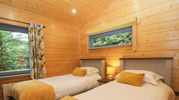A cabin with two beds, each with a pillow and a bedside table with a lamp.