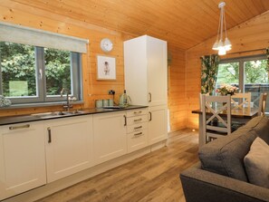 A cabin interior with a kitchen area, dining space, and a sofa. - Oak Lodge (Ulverston)