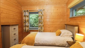 A wooden cabin bedroom with two beds, a dresser, and a window with curtains.