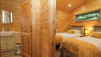 Una cabaña de madera con baño, dos camas con ropa de cama amarilla y un ventanal con vistas al follaje.