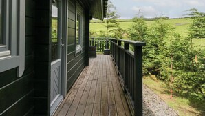 A wooden deck with a green railing, overlooking a green landscape with trees and a field. - Oak Lodge (Ulverston)