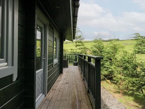 A wooden deck with a green railing, overlooking a green landscape with trees and a field. - Oak Lodge (Ulverston)