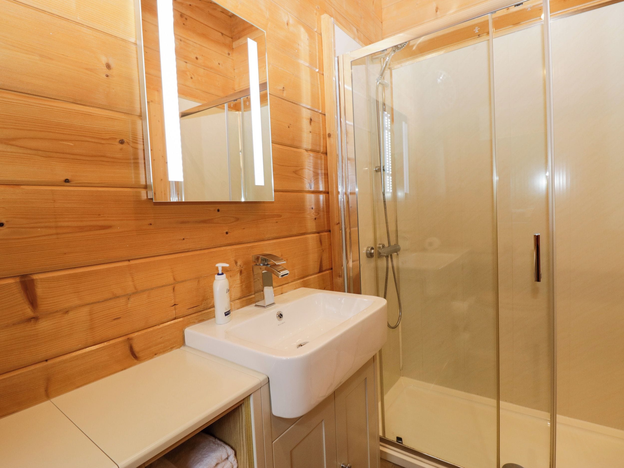 A wooden interior with a white sink, mirror, and glass-enclosed shower.