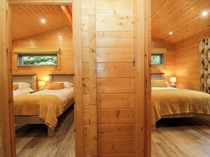 A wooden cabin with two bedrooms, each with a bed, bedside table, and a window. - Oak Lodge (Ulverston)
