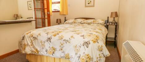 A bedroom with a bed, a bedside table, a lamp, a radiator, a window with curtains, and a mirror.