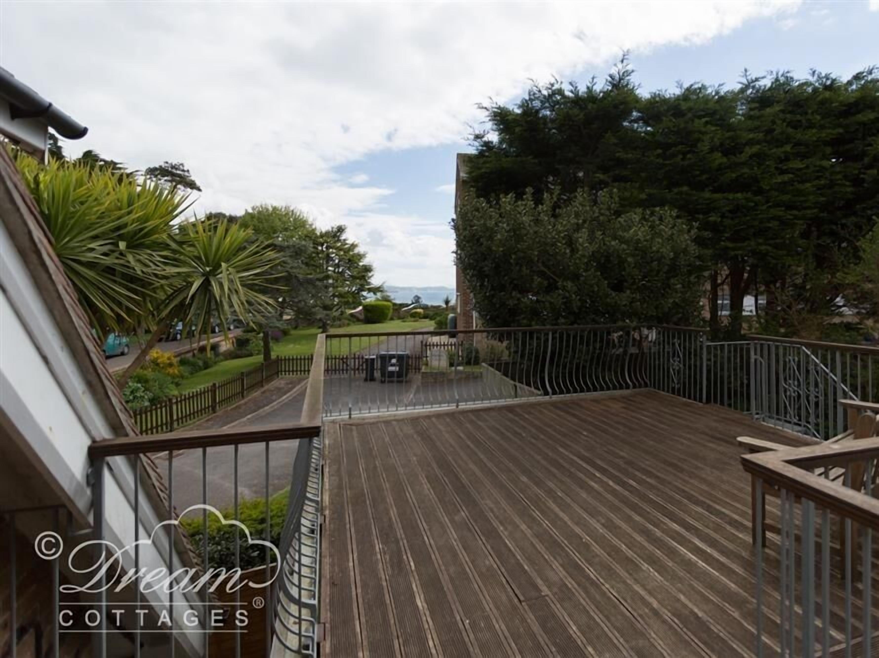 A wooden deck with a metal railing, surrounded by greenery and trees.