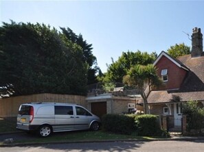 A residential area with a silver van parked in front of a house with a red brick facade, a white door, and a small window.