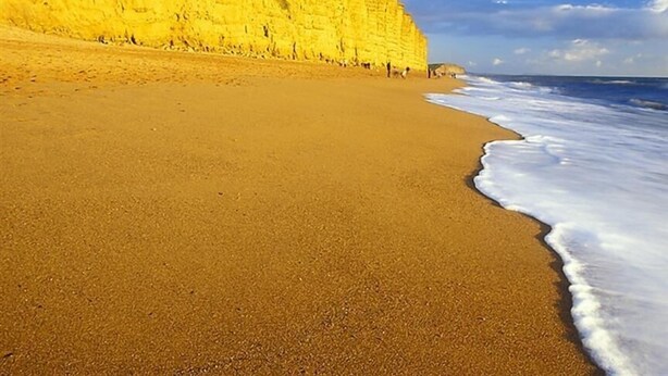 A beach with a large cliff and ocean waves.