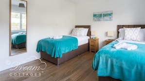 A bedroom with two beds, a mirror, a window, and a ceiling light. - Seacliff (Bridport)