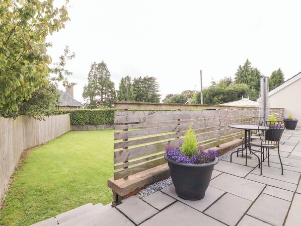 Eine Terrasse mit Holzzaun, Rasen und einer Sitzgelegenheit mit Tisch und Stühlen.